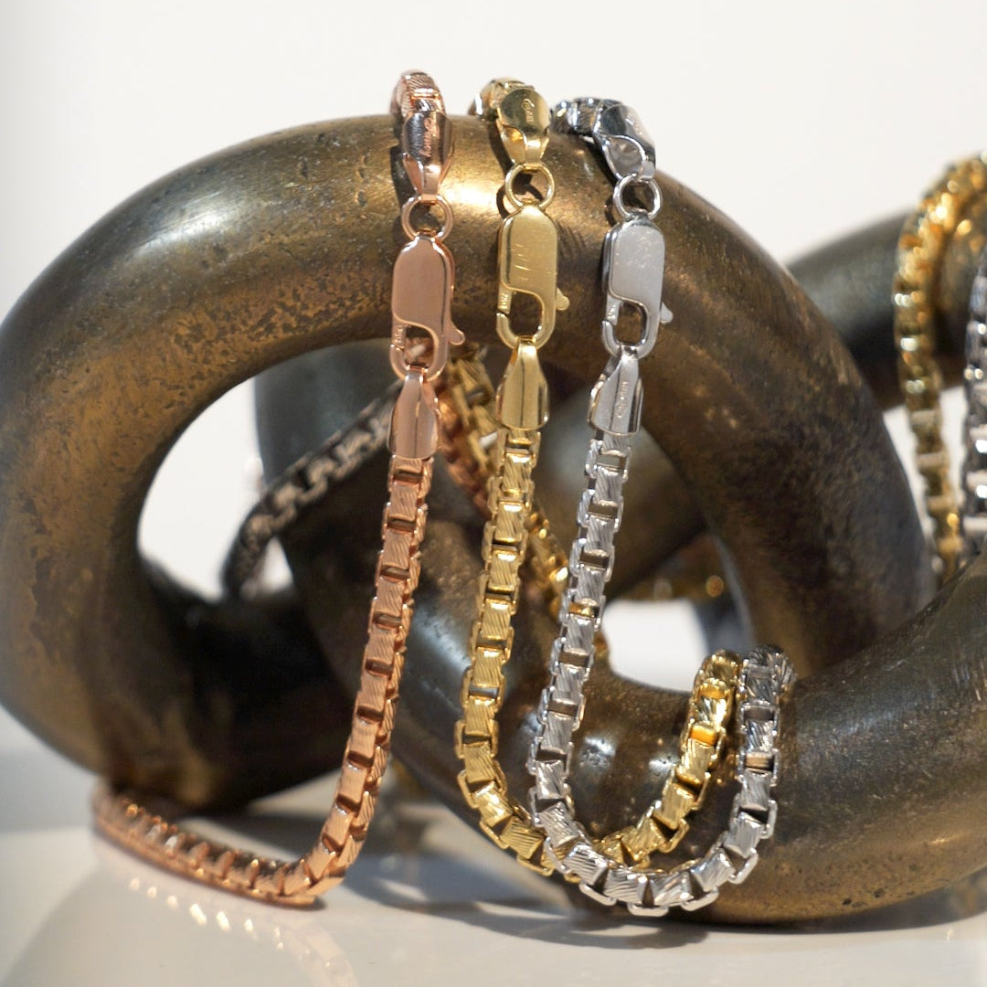Three gold chains on a textured metal surface with a white background
